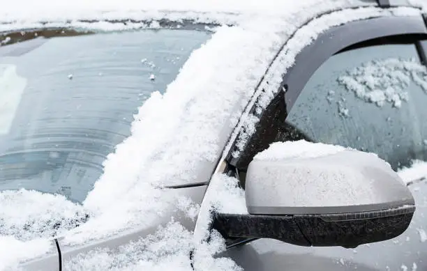 Photo of First snow covered car, close up. Car parked on the street at snowy day.