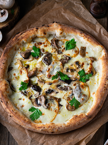 Mushroom pizza with addition mozzarella cheese and herbs on a wooden table. Vertical