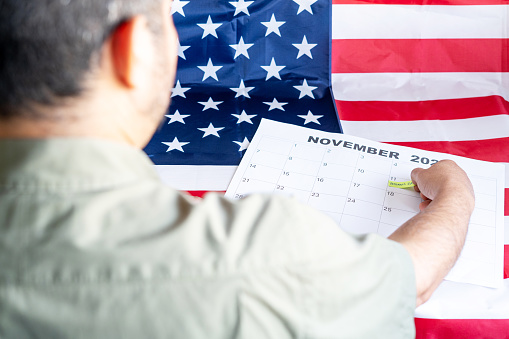 Veteran marking Veteran's Day calendar with the U.S. flag in the background. High quality photo