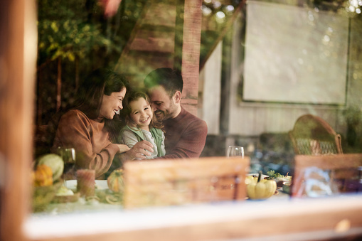Young happy family enjoying during a meal in dining room. The view is through glass.