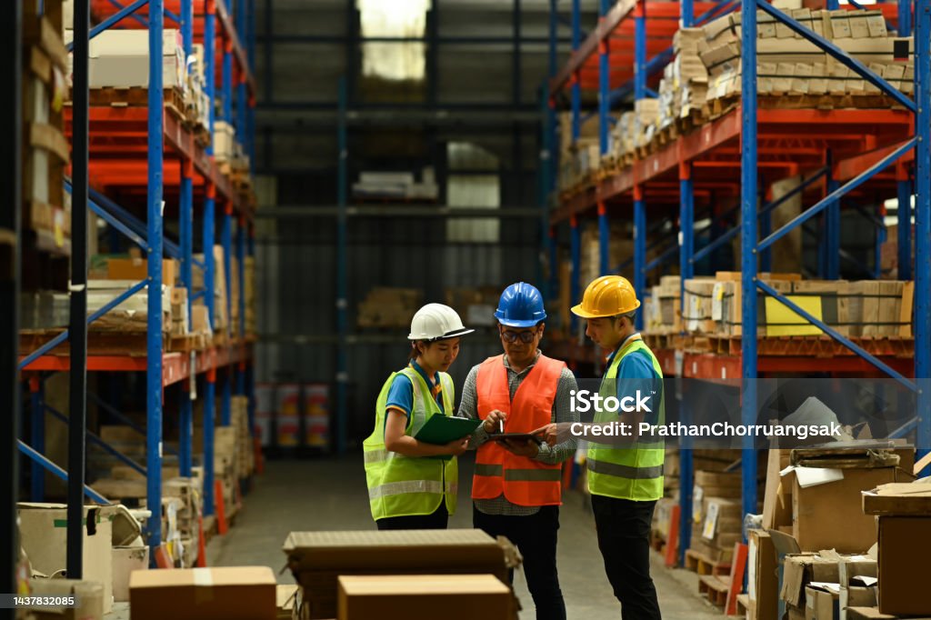Team of manager using digital tablet while standing between retail warehouse full of shelves. Warehouse Stock Photo