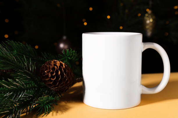 istock White ceramic mug close-up on a beige background with spruce branches and beautiful golden lights. Mockup with copy space for Christmas and New Year. 1437832503