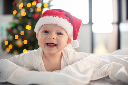 Portrait of a cute ,smiling and joyful baby boy with Santa hat laying in front of the Christmas tree.