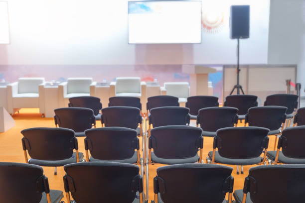 istock Super conference hall with black chairs and colored illumination and blank screen 1437832858