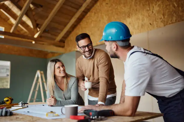 Photo of Happy couple talking to manual worker at construction site.