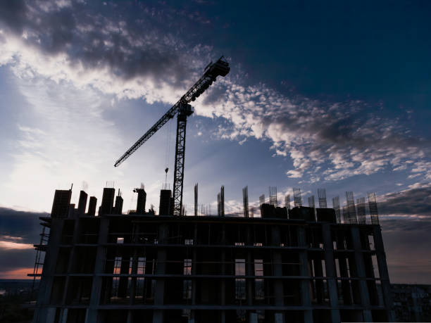 istock Tower crane and building construction site silhouette at sunrise. The construction crane and the building against the blue sky 1437835103