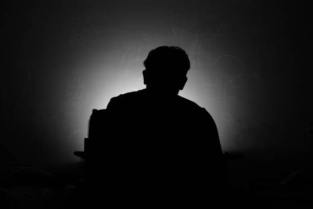 A silhouette of a man from behind looking at a computer scene with symbols floating around him