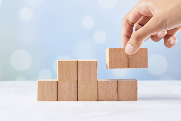 istock Hand adding two wooden blocks to a set of blocks with a blue bokeh light background 1437838588