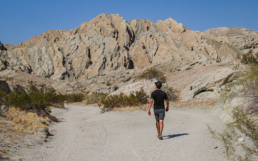 Indio, California, United States – October 18, 2020: A solo male hiker walks toward a rock formation on the Indio Hills Badlands hiking trail.