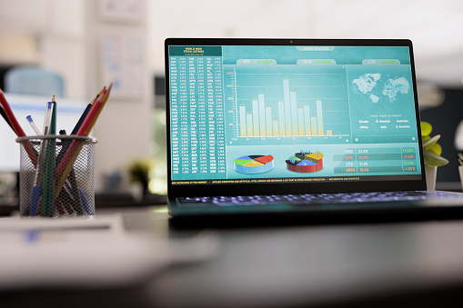 Stock market trade chart on laptop display on wooden table blurred photo background. Investment workplace with trading graphic, interior business marketing trader concept.