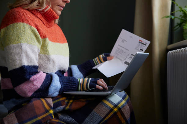 une femme avec un ordinateur portable et bill essayant de se réchauffer par radiateur pendant la crise énergétique du coût de la vie - number 48 photos et images de collection