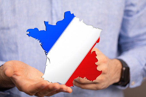 A businessman holding the France map with the French flag colors on it in his hands