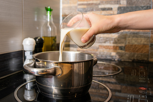 A closeup of a person making oatmeal with milk in a pot on the stove
