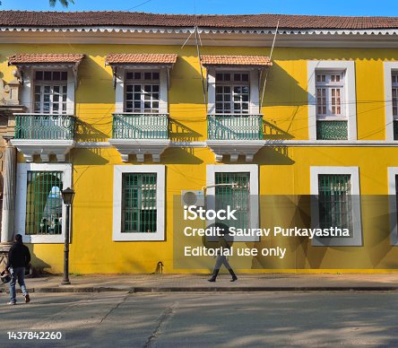 People walking in front of an old, yellow Portuguese house at fontainhas in Panaji, Goa..
