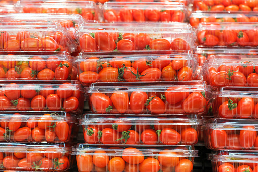 Stacks of red cherry tomatoes in plastic containers close up in a supermarket.