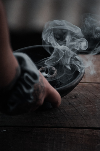 A vertical shot of a hand holding a burning incense in a black bowl