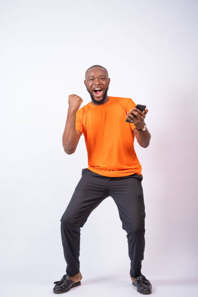istock Excited young Nigerian man celebrates while looking at his phone isolated on a white background 1437844030