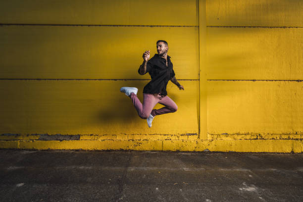 istock Young stylish hot man jumping next to a yellow wall 1437845082