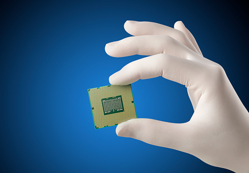 Hand in white glove holding a CPU computer processor microchip on blue background.