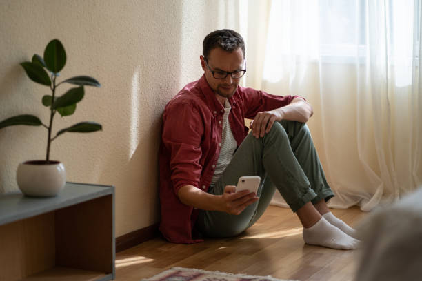 istock Upset young man holding smartphone waiting for ex-girlfriend call while sitting on floor at home 1437846648