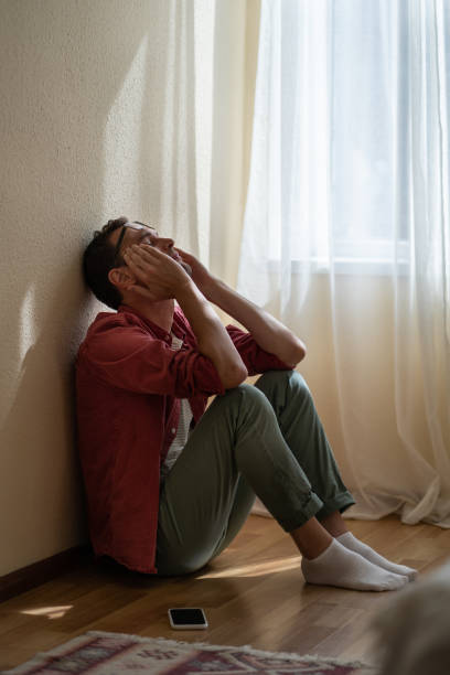 Upset depressed young man sitting on floor at home, received unexpected bad news over phone Upset depressed young man sitting with closed eyes on floor at home, getting unexpected bad news over phone. Frustrated guy suffering from relationship break up, cannot forget about ex-girlfriend unusual couple stock pictures, royalty-free photos & images