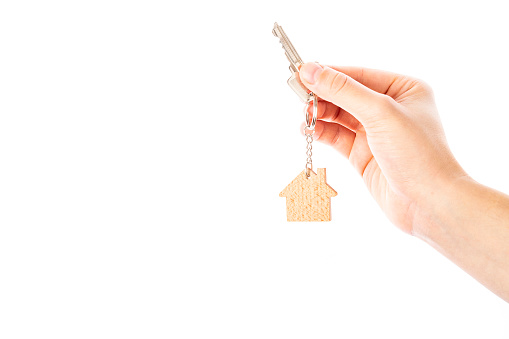 Front view of a white person hand holding a house key with a model house keychain. The hand is at the right side of the image leaving a useful copy space at the left side on a white background