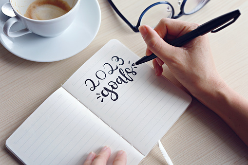 Businesswomen writing 2023 goals on notebook for new year resolution plan.