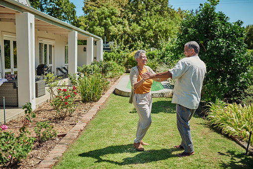 Home, garden and retirement couple dance for wellness, real estate success and celebration with summer outdoor plants in healthy environment. Elderly pension people dancing together in green backyard