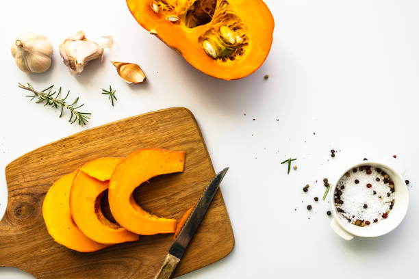 A raw hokkaido pumpkin sliced on a cutting board Vegetables, autumn, preparation, white background, top view, wood, knife, spice squash soup stock pictures, royalty-free photos & images