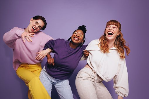 Vibrant multiethnic friends dancing and having fun in a studio. Group of happy female friends celebrating and having a good time against a purple background. Best friends making cheerful memories.