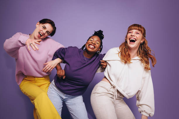 Vibrant multiethnic friends dancing and having fun in a studio Vibrant multiethnic friends dancing and having fun in a studio. Group of happy female friends celebrating and having a good time against a purple background. Best friends making cheerful memories. group of people laughing stock pictures, royalty-free photos & images