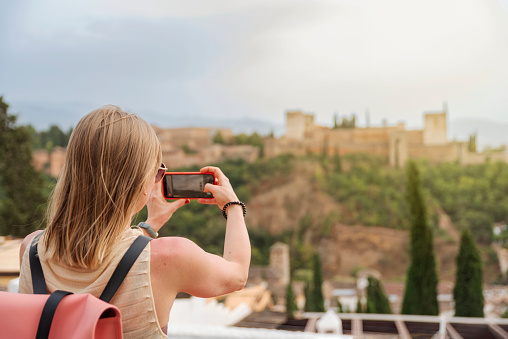 Young blonde female tourist taking the picture of Alhambra in Granada, Spain