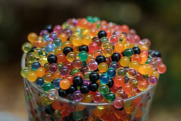 Close up at 45 degrees from above on a glass filled with colored balls. Strong tilt shift effect and strong bokeh.