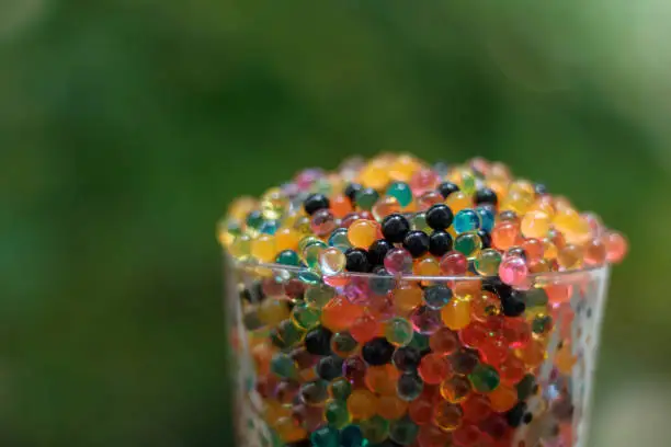 Close up on a glass filled with colored balls. Green bokeh background