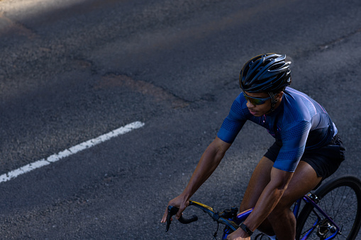 High angle view of young adult cycling on a professional road bike wearing lycra and a helmet on the road. He is determined and concentrates on what he is doing cycling up hill.