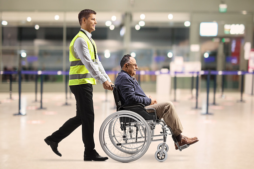 Full length profile shot of an airport worker pushing a mature man in a wheelchair at the airport terminal building