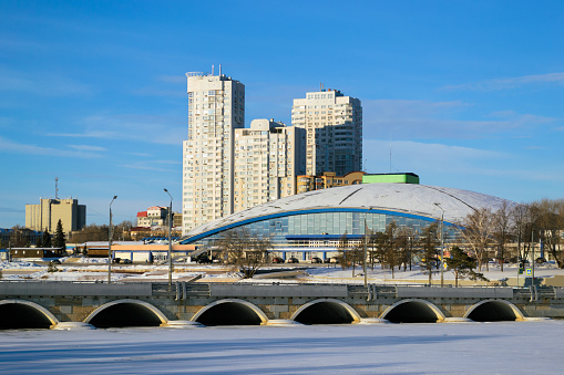 Arched bridge over a frozen river and city buildings illuminated by the sun