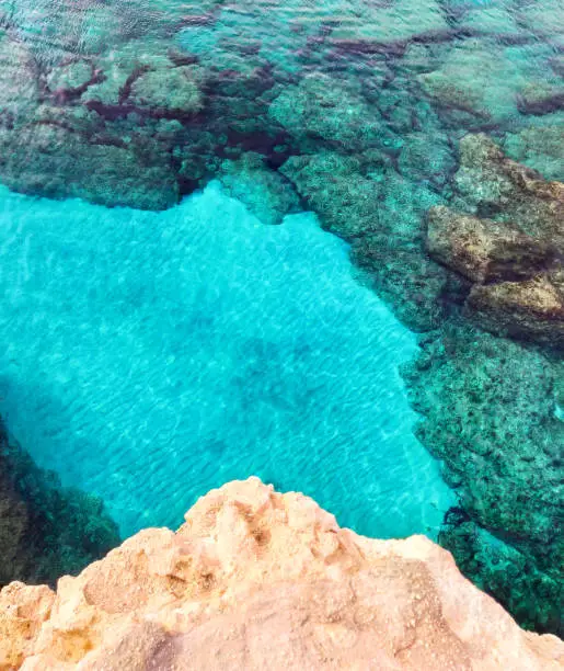 Rocky seabed with clear blue water. Lagre stones in the water, vertical top view. Mediterranean Sea coast near Ayia Napa, Cyprus. Summer sunny landscape.