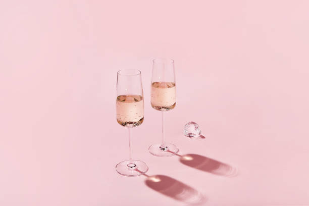 бокалы для игристого вина на розовом фоне. бокалы для шампанского с острыми тенями. современная, стильная цветовая концепция - champagne pink bottle isolated стоковые фото и изображения