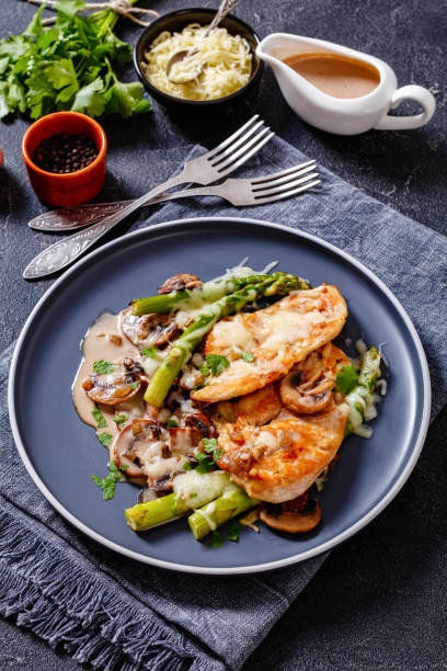 Chicken Madeira served on plate, top view Chicken Madeira, juicy chicken breasts and mushrooms in a madeira cream sauce under melty mozzarella cheese and asparagus on plate, vertical view madeira sauce stock pictures, royalty-free photos & images