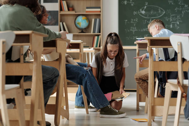 istock Cruel schoolkids laughing at classmate standing on knees in aisle between desks 1437862282