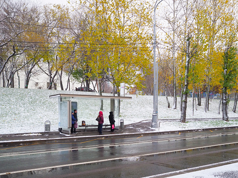 Moscow. Russia. October 31, 2022. People at a public transport stop are waiting for the bus to arrive. The first snowfall in Moscow in autumn 2022.