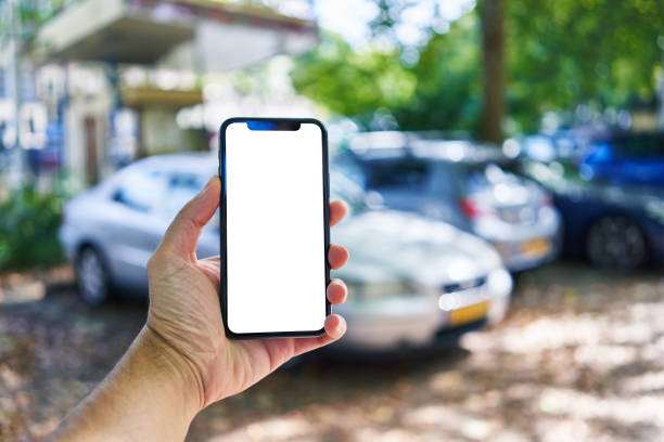 istock Man holding smartphone showing white blank screen at car parking 1437862690