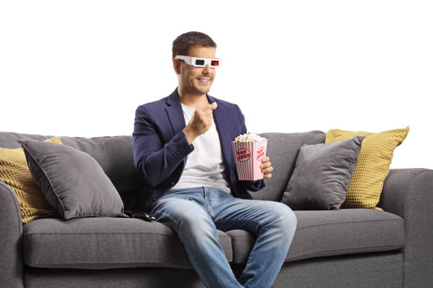 istock Young man with 3d glasses eating popcorn and sitting on a sofa 1437863806