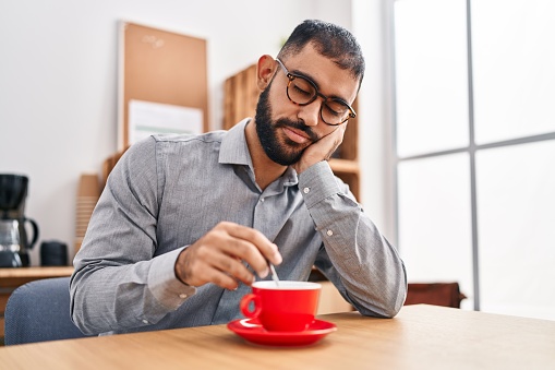 Young hispanic man business worker tired removing coffee at office