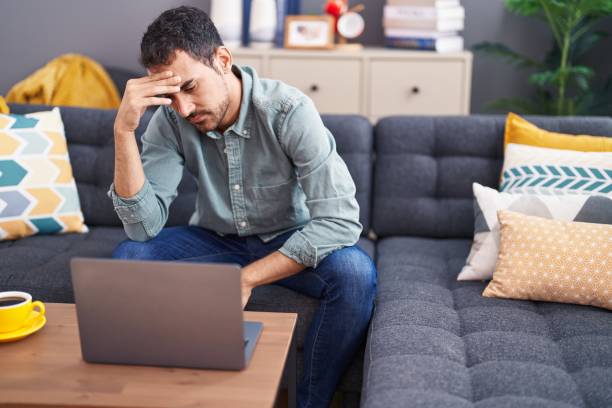 istock Young hispanic man stressed using laptop sitting on sofa at home 1437865319