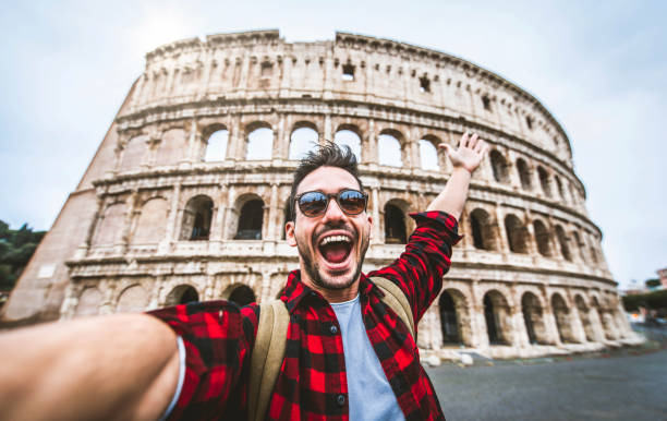 Happy tourist visiting Colosseum in Rome, Italy - Young man taking selfie in front of famous Italian landmark - Travel and holidays concept stock photo