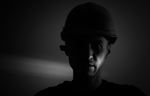 Dirty face of coal miner on a black background. Head of tired mine worker in a hard hat