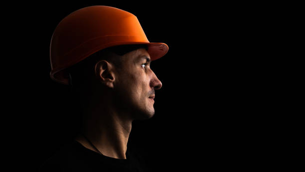 Dirty face of coal miner on a black background. Head of tired mine worker in a hard hat. stock photo