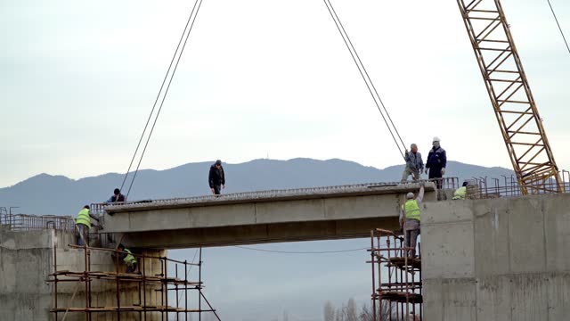 Workers on a road bridge construction site adjusting a big concrete segment of the bridge